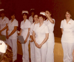 A woman in a white uniform places a nurses cap on a graduate in a white uniform.