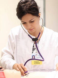 A student uses a stethoscope to examine a Maniken human model.