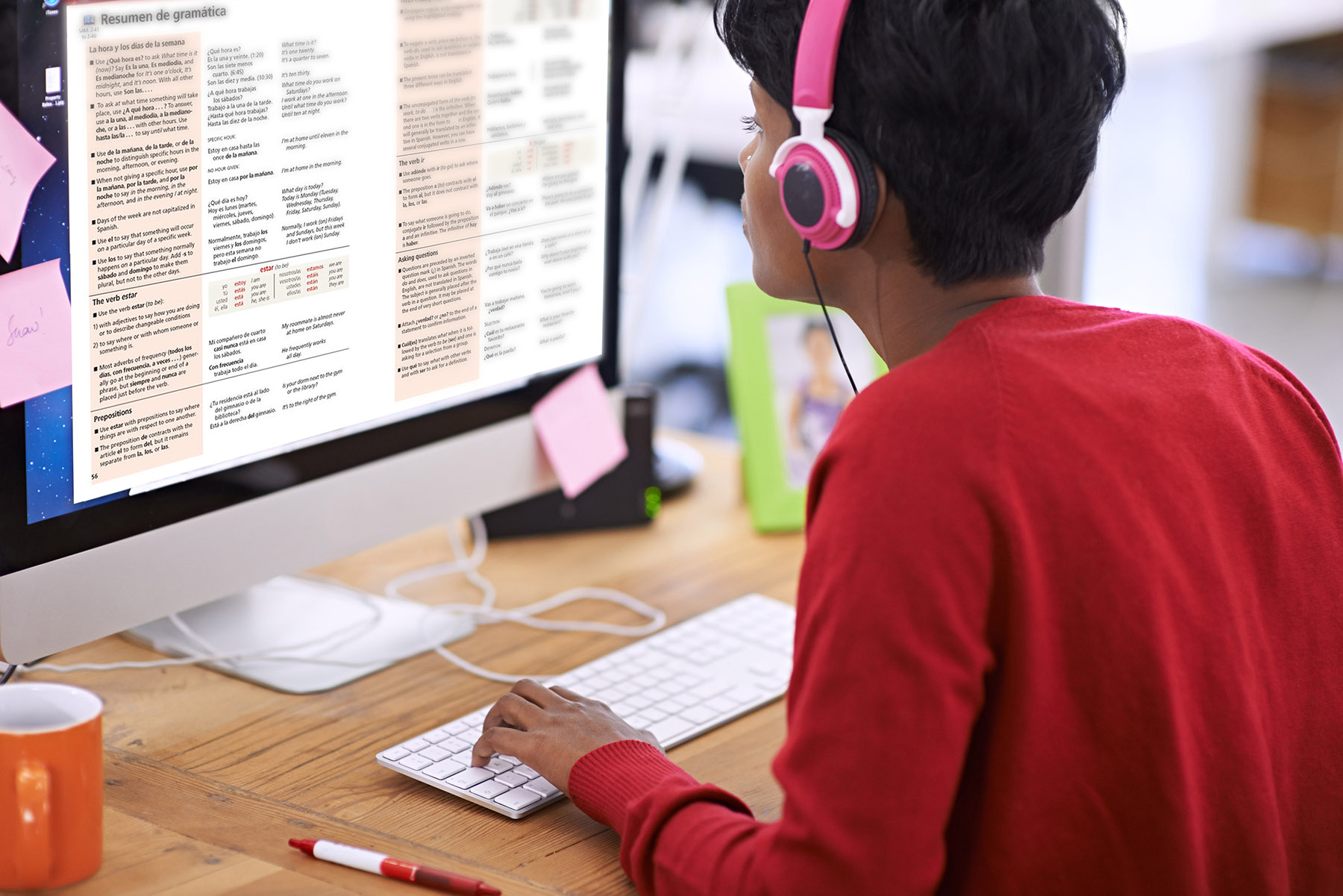 Student wearing headphones and doing Spanish homework on a desktop computer.