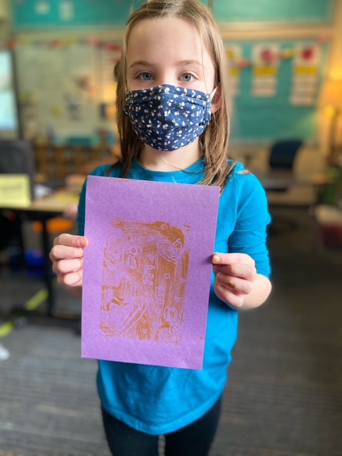 Child in a face mask holds up a red print on purple paper that reads, Freedom.