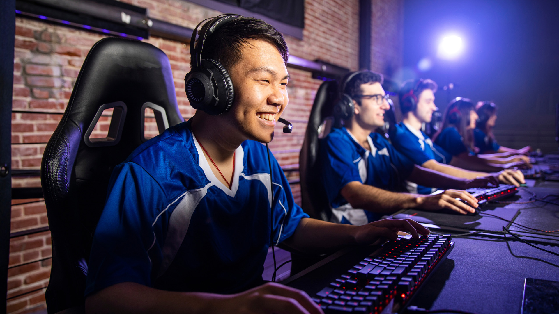 Students in gaming chairs smiling over their computers.