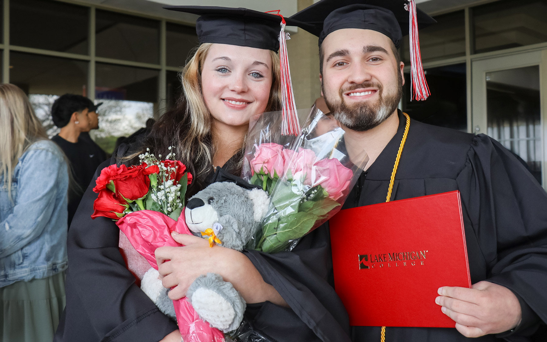 Two graduates smiling with cap and gown, and diploma.