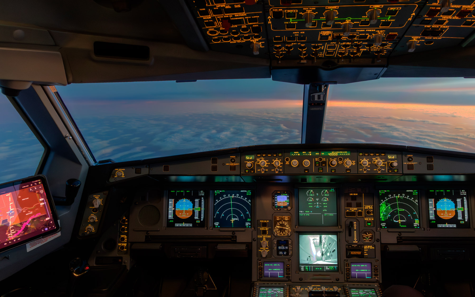 Airplane cockpit view above clouds at sunset.