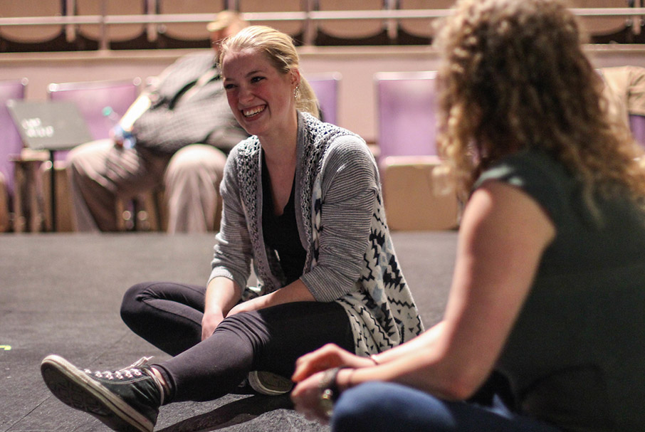 Student and instructor having informal discussion in acting class sitting on stage