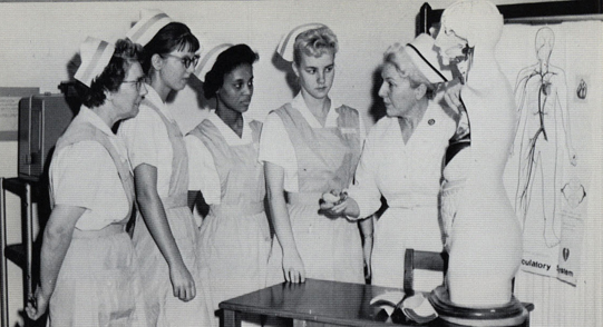 Group of young female nurses stand around an instructor with a mannequin.