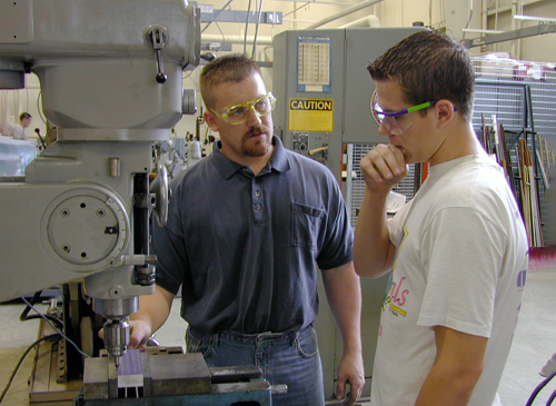 A student and instructor talking near a lathe in machine shop.