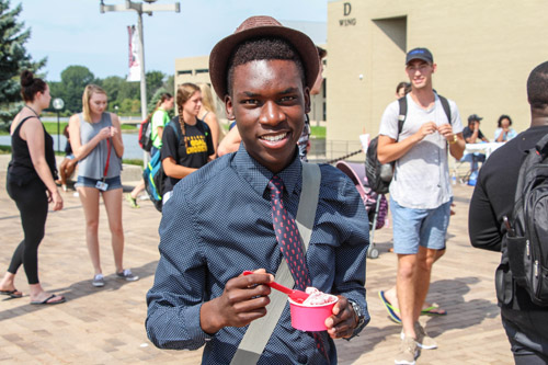 A student poses in front of other students at the entrance to the Benton Harbor Campus, eating ice cream.