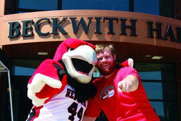 Rocky the Redhawk poses with a student in front of the Beckwith Hall sign over the front door.