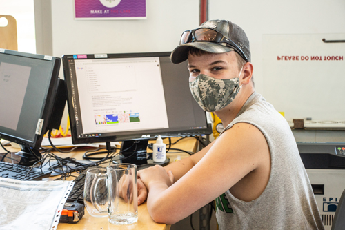A student wearing a mask during the pandemic poses in front of a computer.