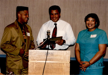 Muhammed Ali posing at a lectern, presenting a folder to a young man.