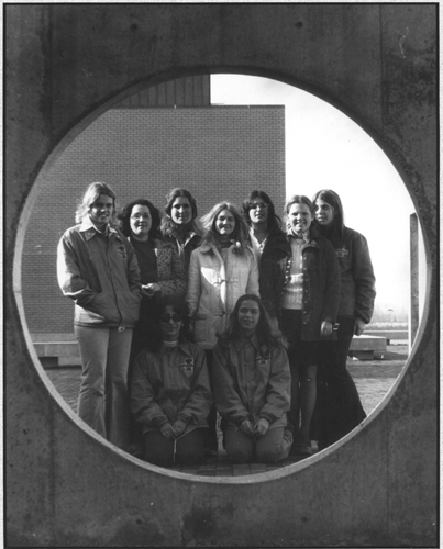 A group of students poses behind a round, concrete window on the Benton Harbor Campus plaza.