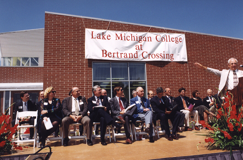 Dignitaries seated in front of a sign reading Lake Michigan College at Bertrand Crossing during the ribbon cutting ceremony.