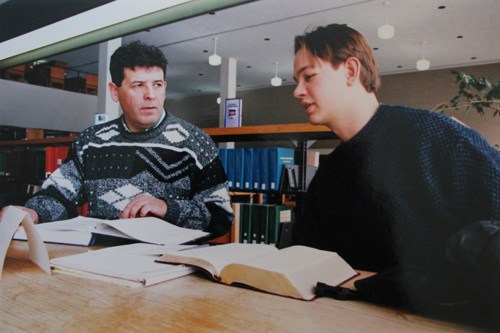 Two students sitting in the library talking over open books.