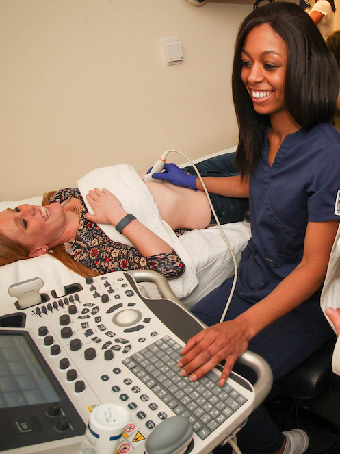 Songraphy student uses machine to practice imaging on a classmate - they are laughing.
