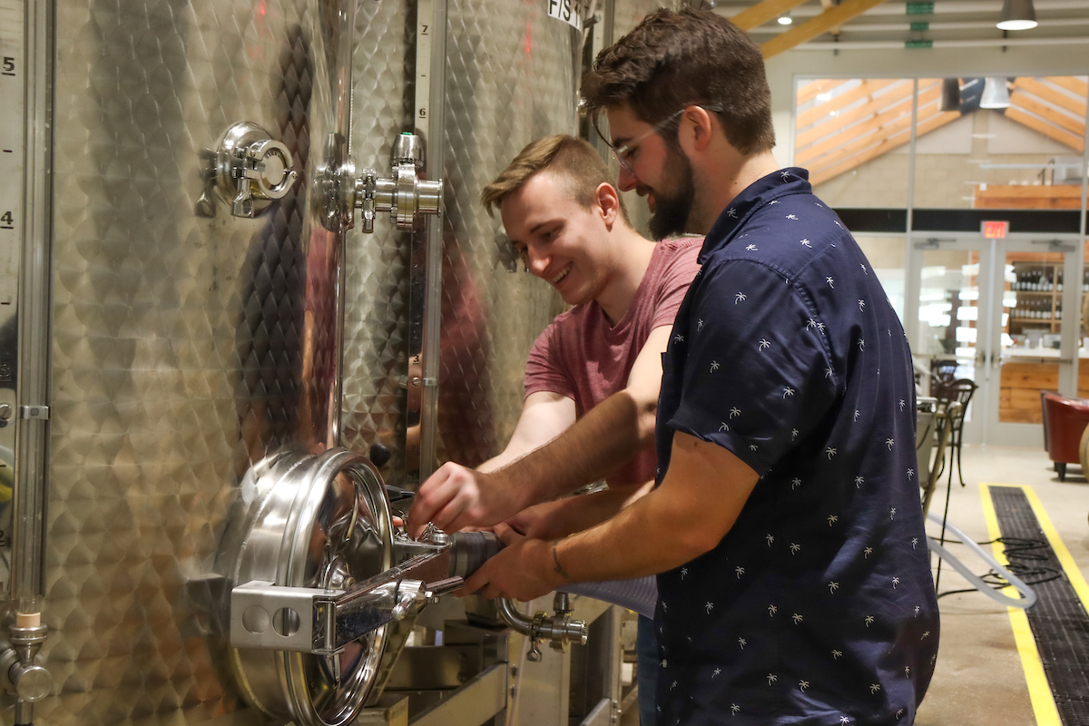 Two enologists working with stainless steel distilling equipment.