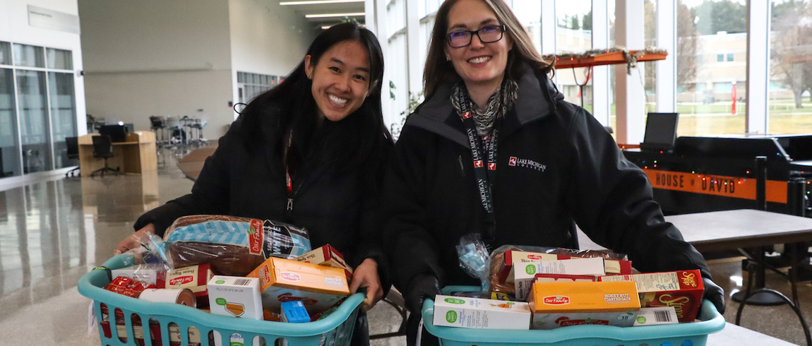  Lake Michigan College employees Anna Bockheim, left, and Laura Henderson-Whiteford carry holiday food baskets prepared for community members in December 2022. 
