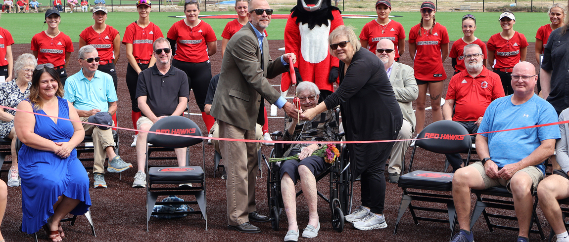 Photo: Jeremy Miller, Liz Miller (seated), and Jennifer Hoover, surrounded by family, Lake Michigan College officials, and the LMC softball team, prepare to cut the ribbon during the dedication ceremony of the Liz and Lloyd Miller Family Field on the LMC Benton Harbor campus. Photo: Jeremy Miller, Liz Miller (seated), and Jennifer Hoover, surrounded by family, Lake Michigan College officials, and the LMC softball team, prepare to cut the ribbon during the dedication ceremony of the Liz and Lloyd Miller Family Field on the LMC Benton Harbor campus.