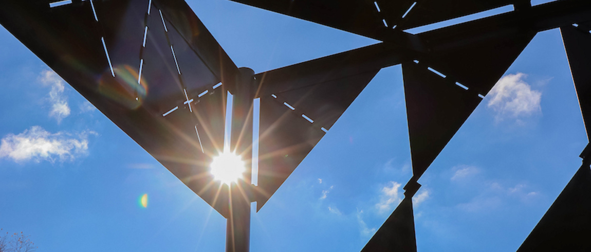 Sun shines through a geometric sculpture against a blue sky. 