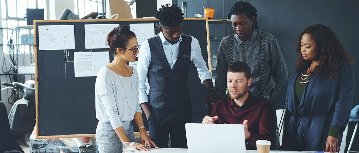 Five individuals in office attire gather at a work table.