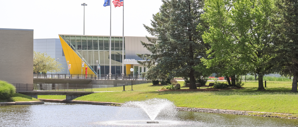 Campus photo of buildings, flags, trees, pond
