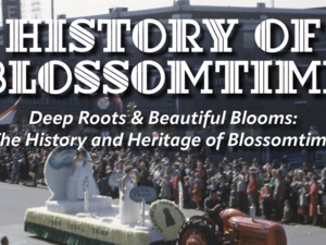 Decorative title slide reading “History of Blossomtime: Deep Roots & Beautiful Blooms—The History and Heritage of Blossomtime” over a vintage photo of a parade. A tractor pulls a flower-covered float past large crowds lining a downtown street, with ornate floral graphics on each side of the title.