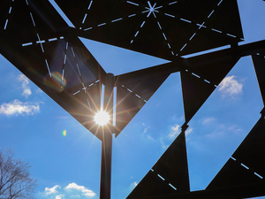 Sun shines through a geometric sculpture against a blue sky. 
