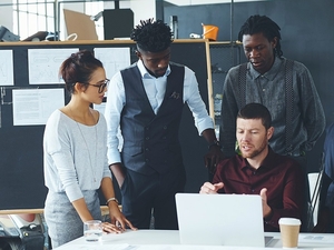 Five individuals in office attire gather at a work table.