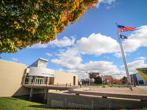 Campus building on a sunny day with blue sky, trees, flags. 