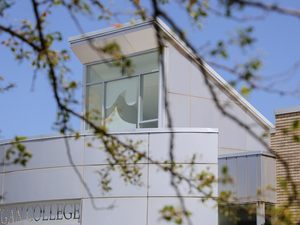 Campus building with blue sky in background, tree branches in foreground, wave logo in building window.