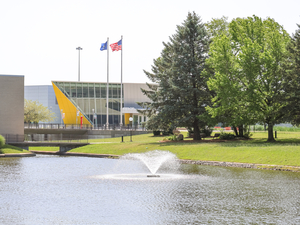 Campus photo of buildings, flags, trees, pond