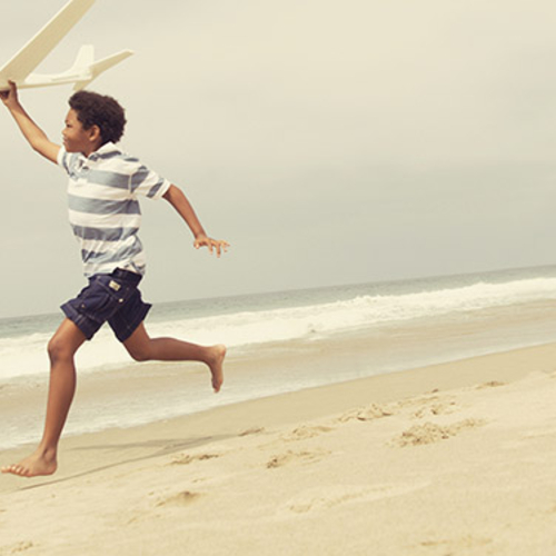 Child playing with toy airplane on the beach.